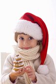 Girl in Father Christmas hat holding biscuit Christmas tree