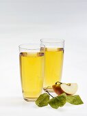 Two glasses of apple juice, wedge of apple and leaves