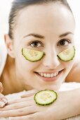 Young woman with cucumber slices under her eyes & on her hand