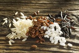 Various types of rice grains on wooden board (long-grain, Camargue, short-grain, wild)