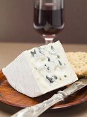 Piece of blue cheese, knife & crackers on wooden plate, red wine