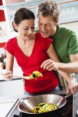 Woman offering man fried vegetables on spatula