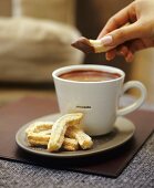 Someone dipping a sugared pastry into hot chocolate