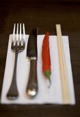 Knife, fork, chilli and chopsticks on napkin
