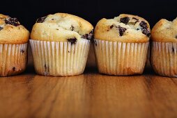 Four chocolate chip muffins in a row on a wooden background