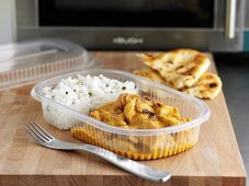 Indian ready-meal in plastic container in front of microwave oven