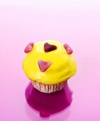 Muffin mit gelbem Zuckerguss und Fruchtgummi-Herzen