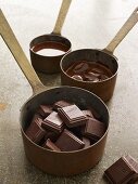 Schokoladenstücke und geschmolzene Schokolade in Töpfen