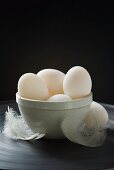 Several duck eggs in ceramic basin, feathers beside it