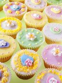 Lots of pastel-coloured fairy cakes decorated with sugar flowers
