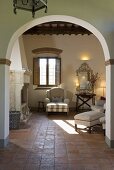 View through an archway on light colored upholstered furniture and tile floor of a country home