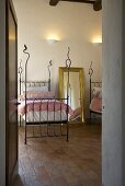Blick durch offene Tür in Schlafraum mit schmiedeeisernem Einzelbett auf Terrakottaboden