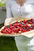 A woman holding a mascarpone tart with fresh berries