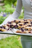 Frau hält Backblech mit Heidelbeer-Butterkuchen