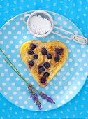 A heart-shaped blueberry pancakes with icing sugar and lavender flowers