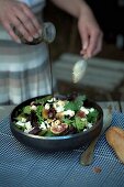 Pouring vinaigrette on green salad with roasted figs and marinated sheep's cheese