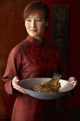 Frau serviert Karpfen aus dem Wok (China)