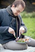 A man sitting on a picnic blanket eating grilled fish