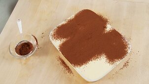 Tiramisu zubereiten: mit Kakaopulver bestäuben