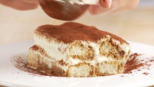 A piece of tiramisu being dusted with cocoa powder