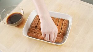 Tiramisu being prepared: espresso-soaked sponge fingers being placed in a dish