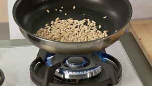 Pine nuts being added to a non-stick pan and roasted