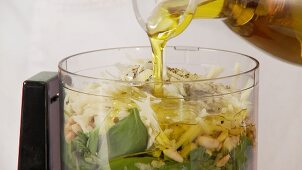 Olive oil being added to pesto ingredients in a mixer