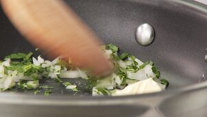 Chopped onions and parsley being added to a pan