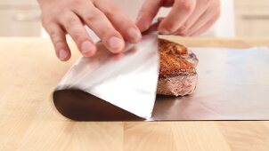 Fried duck breast being wrapped in aluminium foil