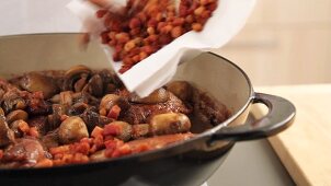 Fried bacon being added to coq au vin