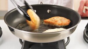 Breaded chicken breasts being fried on both sides