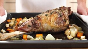 Roasted leg of lamb with vegetables on a baking tray