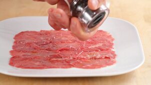 Beef carpaccio being seasoned with salt and pepper