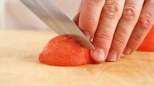 A peeled tomato quarter being diced