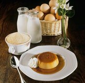 Crème Caramel auf Teller vor Zutaten (Eier, Milch, Mehl)