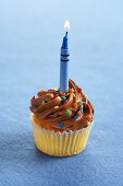 A Yellow Cupcake with Chocolate Frosting, Colored Sprinkles and a Lit Crayon Shaped Candle