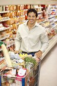 Smiling man pushing full shopping trolley in a supermarket
