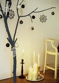 A branch decorated for Christmas next to a tray of candles