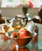 Apples in a silver bowl with a teapot in the background