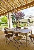 Überdachte Gartenterrasse mit einfachem Vintage-Holztisch, Klappstühlen mit Sitzkissen und einem Kronleuchter