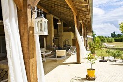 Großes Landhaus mit holzüberdachter Gartenterrasse und wehenden Vorhängen im heißen Sommerwind