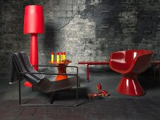 Red floor lamps and a bowl chair on a dark flagstone floor in front of a weathered, grey stone wall