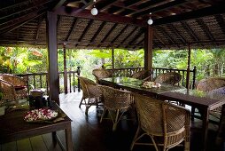 Überdachter Terrassenplatz mit Korbmöbel und Kugelleuchten in tropischer Umgebung