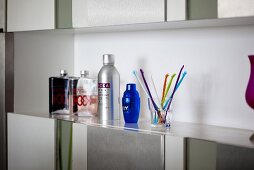 Flagons, bottles and a glass of coloured sticks on a shelf above a built-in cupboard