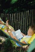 Mädchen liegt mit einem Buch in einer Hängematte im Garten