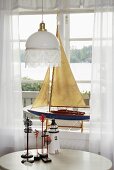 A white ceiling lamp above a table next to a window and a model boat displayed on a window sill