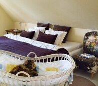 Bett mit violetter Tagesdecke unter Dachschräge und Katze im Kinderbett