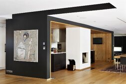 A view through an open-plan kitchen into a living room with black walls and a fireplace in front of a kitchen counter