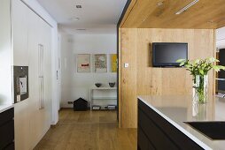 An open-plan kitchen with a counter in front of a wooden partition wall and view of a shelf in an anteroom