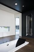 Schwarz-weisses Designer Bad mit Badewanne im Boden eingelassen und Handtuchtrockner an schwarzer Wand